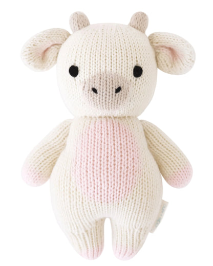 A knitted plush toy shaped like a strawberry cow, featuring a white and pink body, black eyes, beige snout, and small horns—expertly crafted by Cuddle + Kind from heirloom-quality Peruvian cotton yarn for softness and durability. This is the Strawberry Cow - Baby 7".