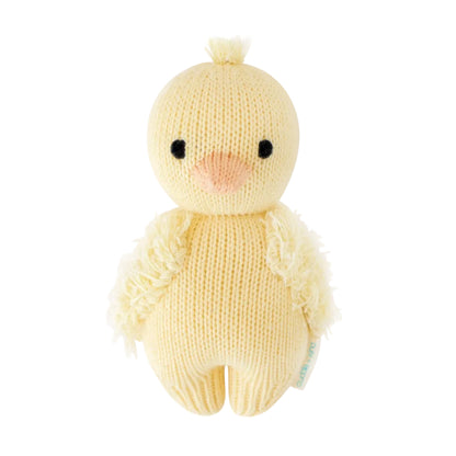 The Baby Duckling by Cuddle + Kind is a handcrafted plush chick toy, made from Peruvian cotton yarn and featuring black eyes, a peach beak, and textured wings in a cheerful yellow hue. Inspired by classic heirloom baby animals, it is displayed against a white background.