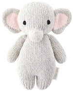The Baby Elephant by Cuddle + Kind is a hand-knit plush toy crafted from heirloom-quality Peruvian cotton yarn, featuring large ears, black eyes, and a soft texture. Shown on a plain white background.