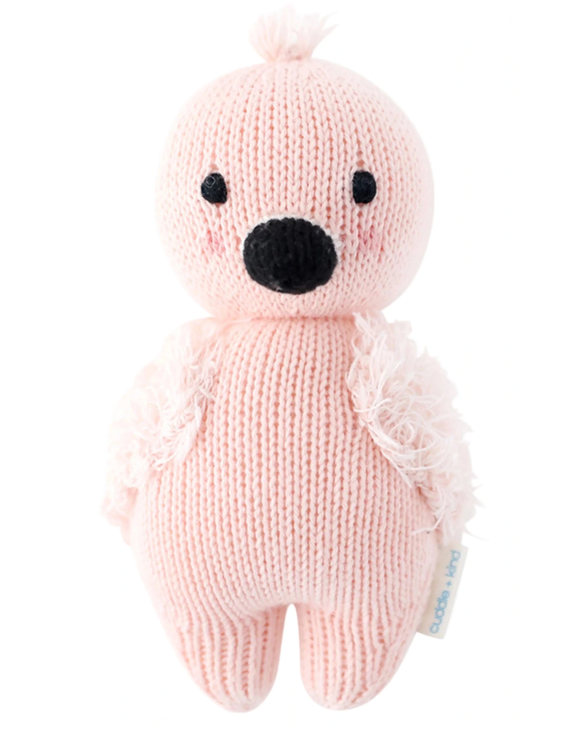 The Baby Flamingo by Cuddle + Kind is a pink hand-knit plush bird with a black beak and eyes, featuring soft textured wings and crafted from Peruvian cotton yarn. It stands upright against a white background.