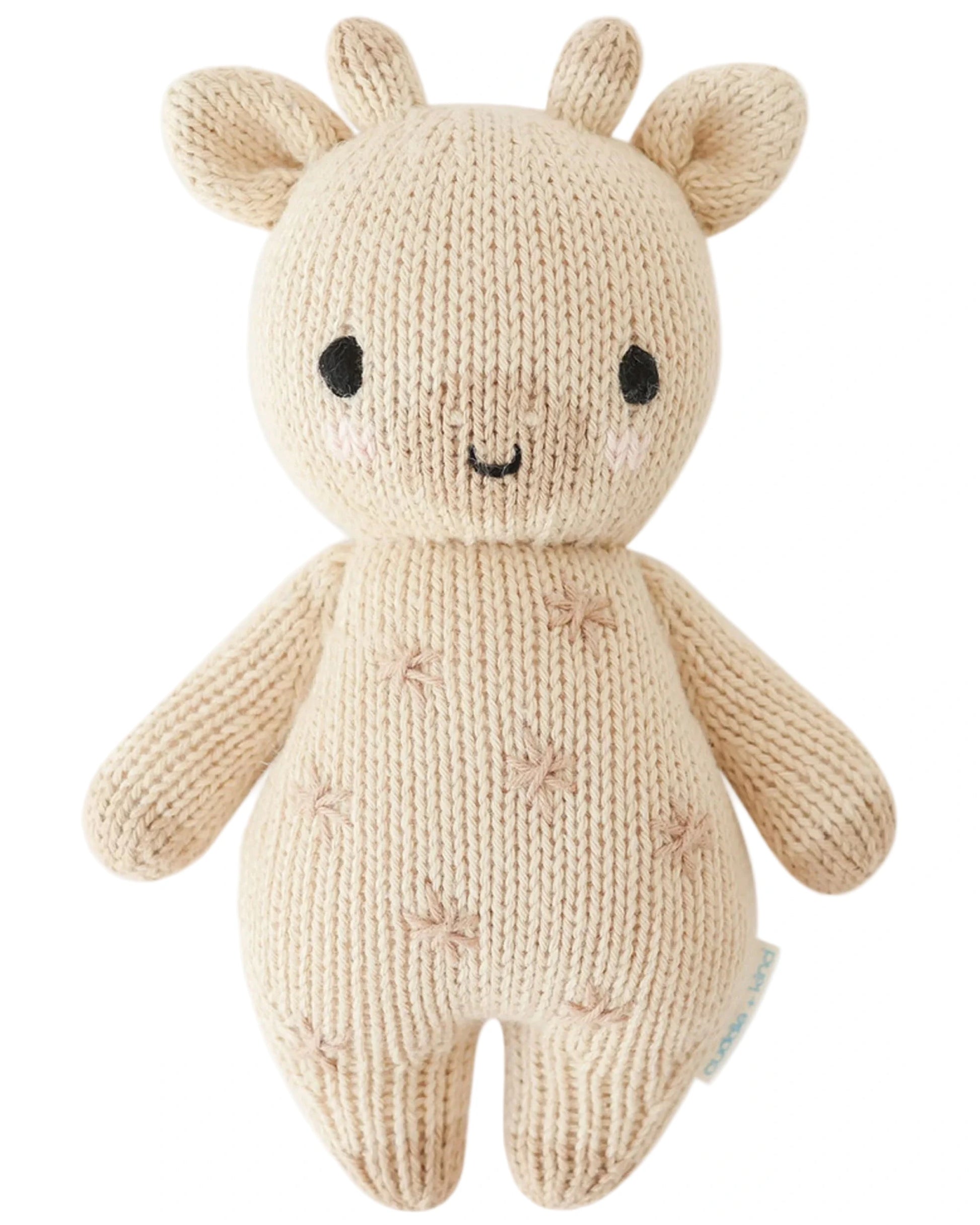 The Baby Giraffe by Cuddle + Kind is a beige knitted plush giraffe made from heirloom-quality Peruvian cotton yarn, with stitched facial details, small horns, and a cheerful smile.