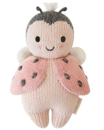 The Baby Ladybug by Cuddle + Kind is an heirloom-quality knitted plush toy featuring a smiling face, pink wings with black spots, and white antennae.