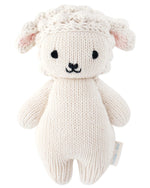 The Cuddle + Kind Baby Lamb is a cream, hand-knit stuffed toy with black embroidered features, textured ears, and a side tag—an heirloom-quality cotton animal perfect for any plush collection.