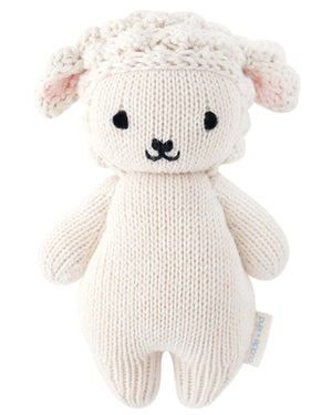 The Cuddle + Kind Baby Lamb is a cream, hand-knit stuffed toy with black embroidered features, textured ears, and a side tag—an heirloom-quality cotton animal perfect for any plush collection.