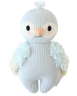 The Sky Blue Parrot - Baby 7" by Cuddle + Kind is a knitted stuffed animal shaped like a bird, featuring light blue heirloom-quality Peruvian cotton yarn, a white face, tufted head, and fluffy wings—shown on a white background.