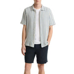 A man wearing the vince Playa Stripe Shortsleeve Shirt over a white tee with dark shorts, standing with one hand in his pocket against a white background.