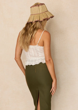 A woman stands with her back to the camera, wearing the Lorna Murray Luxe Beauty Point Hat—a UPF 50+ straw travel hat—paired with a white lace top and a high-waisted olive green skirt featuring a back slit.
