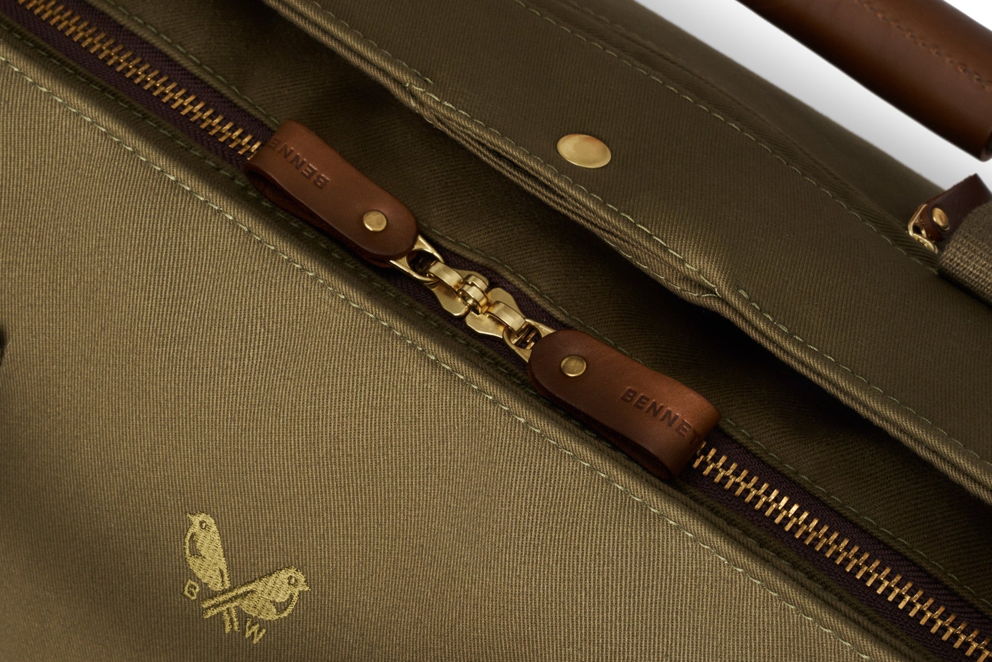 Close-up of the Bennett Winch S.C Holdall featuring its brown leather zipper with gold detailing and a small bird logo, crafted from waterproof khaki canvas.