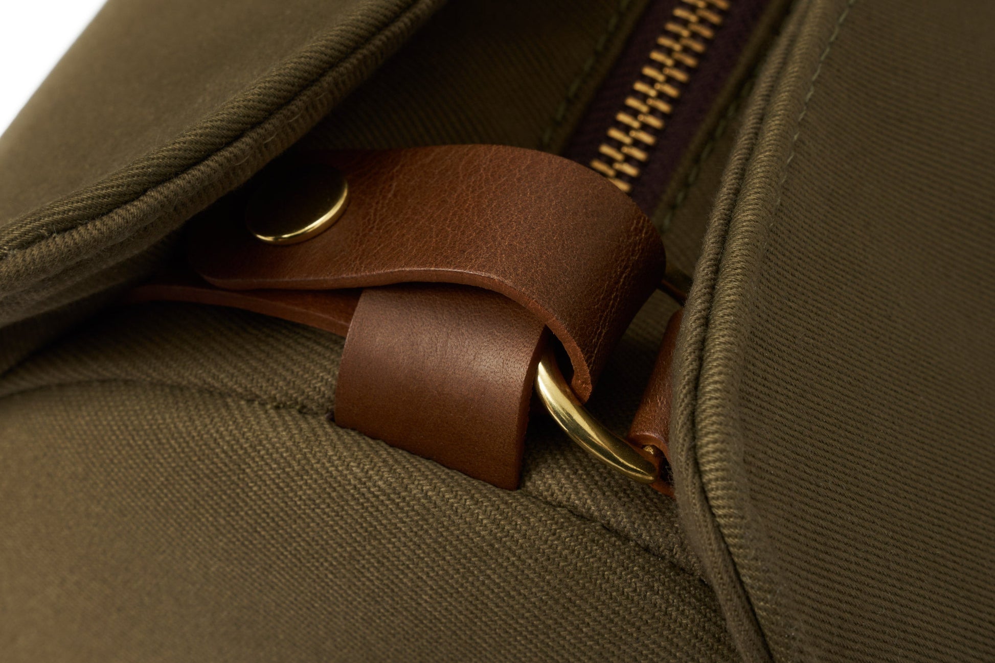 Close-up of the Bennett Winch S.C Holdall in green fabric, featuring a visible brown leather strap and metal ring. A partially open zipper highlights its perfect blend of style and functionality.