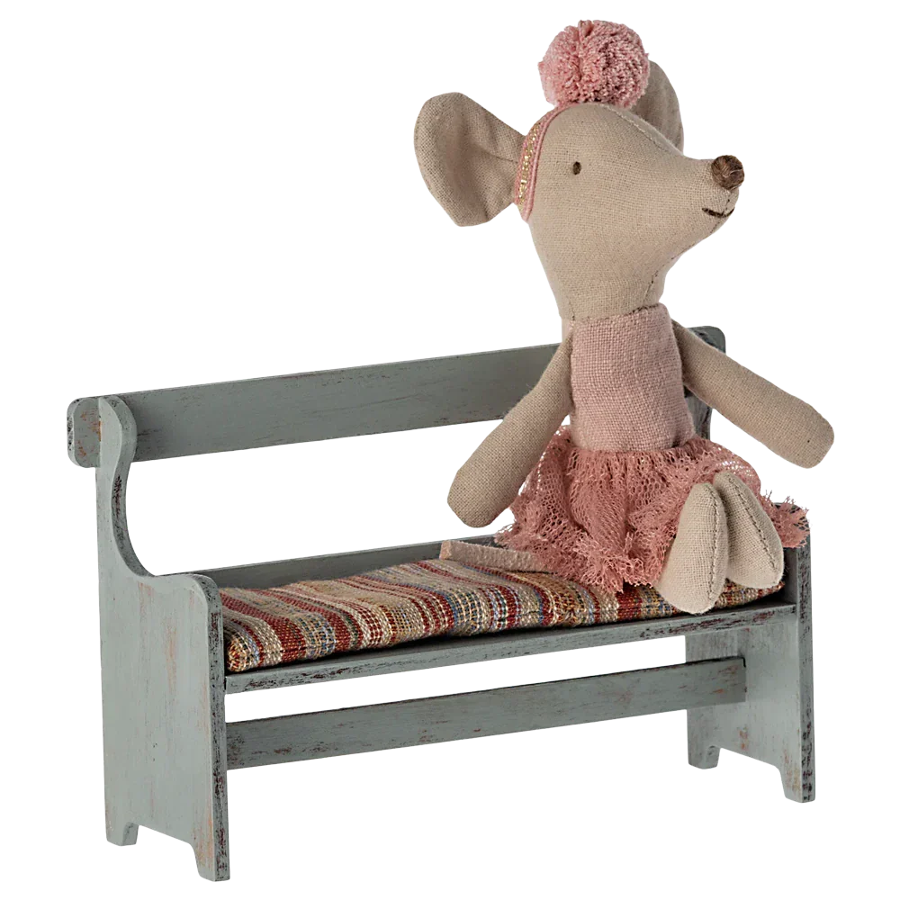 A Maileg fabric mouse doll in a pink outfit sits on the charming Maileg Bench, Mouse with a colorful striped cushion, perfect for adding charm to your Mouse Hole Farmhouse.