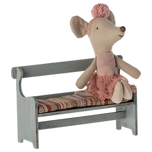 A Maileg fabric mouse doll in a pink outfit sits on the charming Maileg Bench, Mouse with a colorful striped cushion, perfect for adding charm to your Mouse Hole Farmhouse.