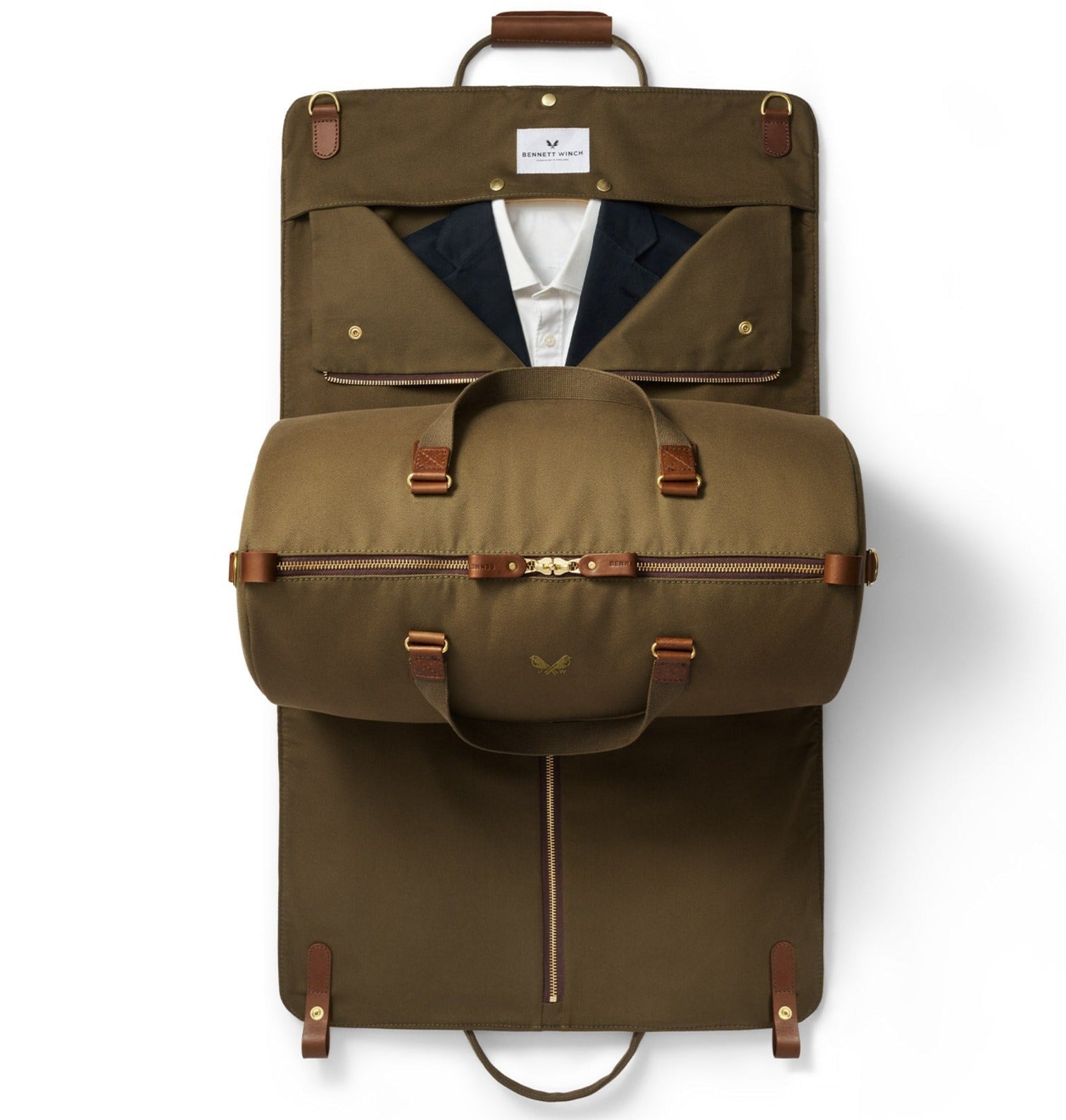 The Bennett Winch S.C Holdall, a green garment bag crafted from waterproof canvas with brown leather straps, is open and reveals a jacket and shirt inside. The holdall-style bag is rolled and zipped halfway.