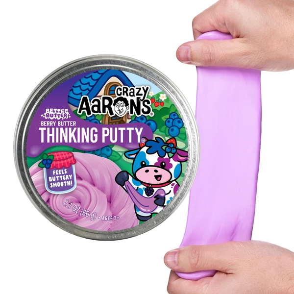 A tin labeled “Crazy Aaron’s Better Butter - Berry Thinking Putty” features a cartoon cow and contains berry-scented, light purple putty. A hand is stretching the soft Thinking Putty next to the tin, making it perfect for sensory play.