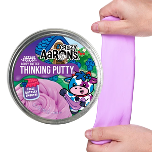A tin labeled “Crazy Aaron’s Better Butter - Berry Thinking Putty” features a cartoon cow and contains berry-scented, light purple putty. A hand is stretching the soft Thinking Putty next to the tin, making it perfect for sensory play.