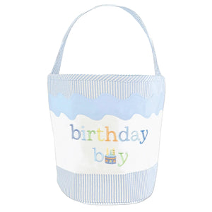 The Birthday Boy Tote by Bits & Bows features light blue and white stripes, a handle, "birthday boy" embroidery, and a cute cake illustration—ideal for gifting or charming toy storage.