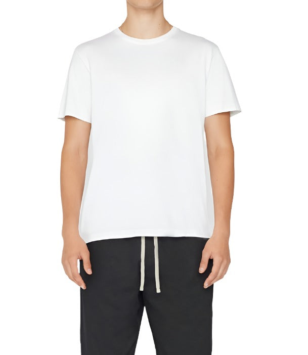 A person dressed in a Frame Men's Logo Tee by Frame and black drawstring pants is standing against a plain background.