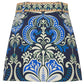 The Blaze Skirt by Cara Cara showcases a chic blue, white, and green floral A-line design with a woven tan raffia belt waistband.