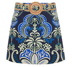 The Blaze Skirt by Cara Cara is a chic A-line mini with a bold blue, green, and cream baroque print, finished with a raffia belt and round buckle.