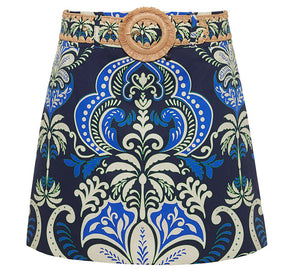 The Blaze Skirt by Cara Cara is a chic A-line mini with a bold blue, green, and cream baroque print, finished with a raffia belt and round buckle.