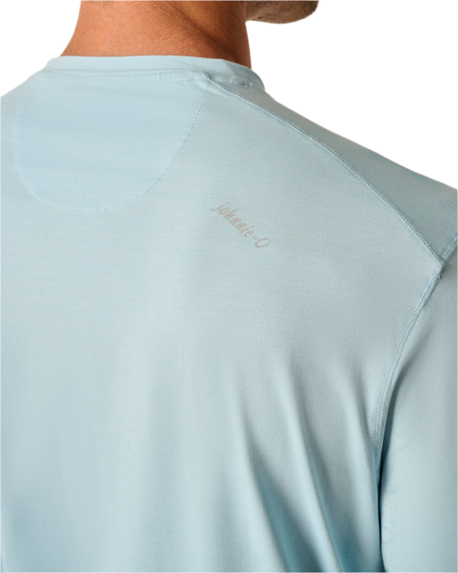 Close-up of someone wearing a Johnnie-O Basin Performance Sun Shirt in light blue, featuring subtle branding on the upper back. It's ideal for beach days, keeping you cool with SPF 50 protection.