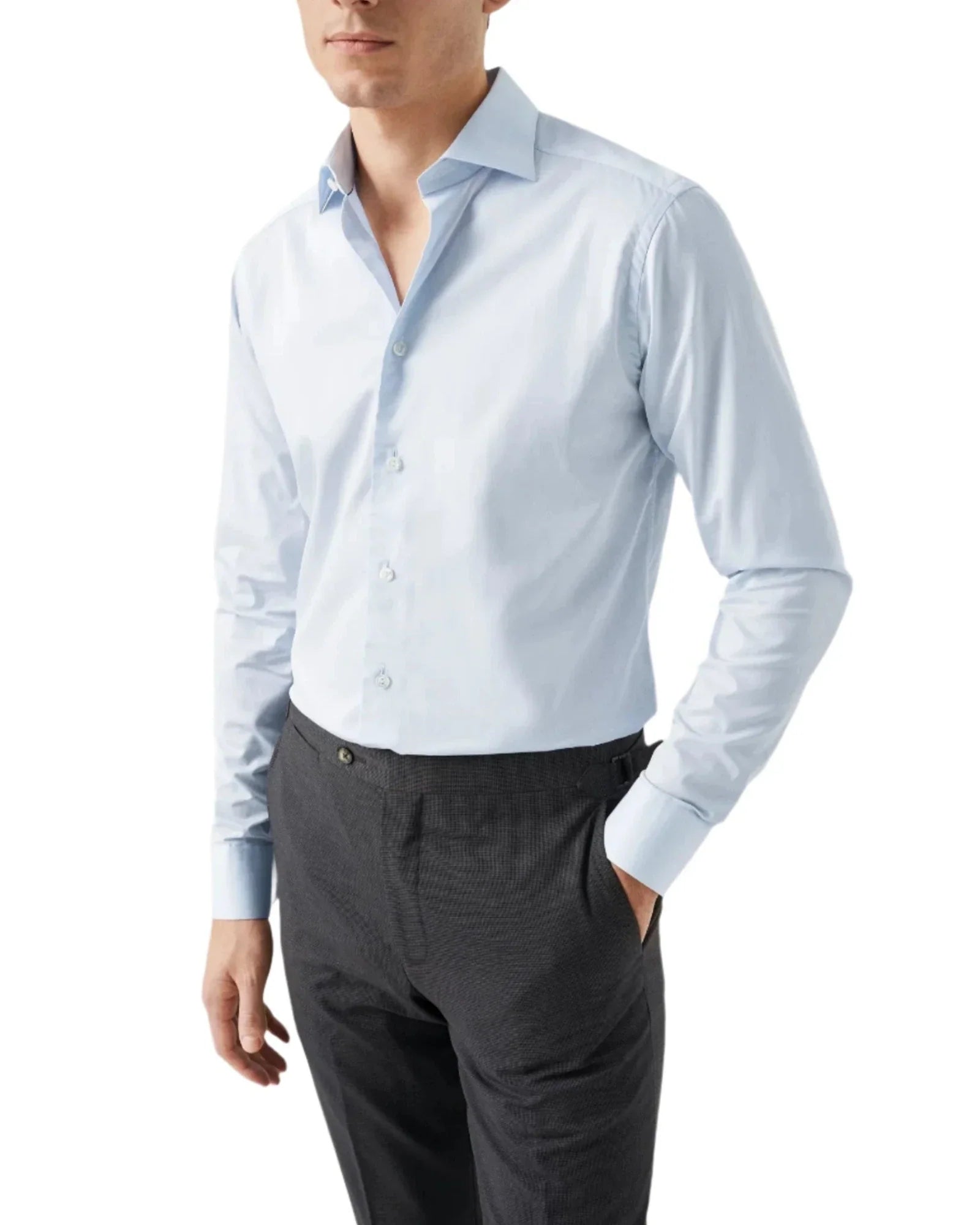 A person wearing an Eton Solid Elevated Twill Shirt in light blue and dark gray trousers stands confidently with one hand in a pocket. The Eton shirt, made from crease-resistant organic cotton, features a button-up front and a classic collar, offering both style and comfort.