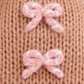 Close-up of the Baby Gingerbread - Candy Swirl by Cuddle + Kind, showcasing a knitted brown fabric with two small pink and white yarn bows, meticulously handcrafted from heirloom-quality Peruvian cotton for a soft and cherished baby companion.