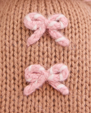 Close-up of the Baby Gingerbread - Candy Swirl by Cuddle + Kind, showcasing a knitted brown fabric with two small pink and white yarn bows, meticulously handcrafted from heirloom-quality Peruvian cotton for a soft and cherished baby companion.