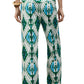 A person stands with their back to the camera, wearing Figue's Justine Pant featuring a blue and green geometric print, side pockets, and a drawstring waist, paired with the matching top, tan sandals, and a chunky bracelet.