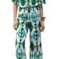 Woman wears the Figue Bodhi Top, a V-neck patterned piece with blue, green, and white geometric designs, paired with fringe sandals and a bracelet.