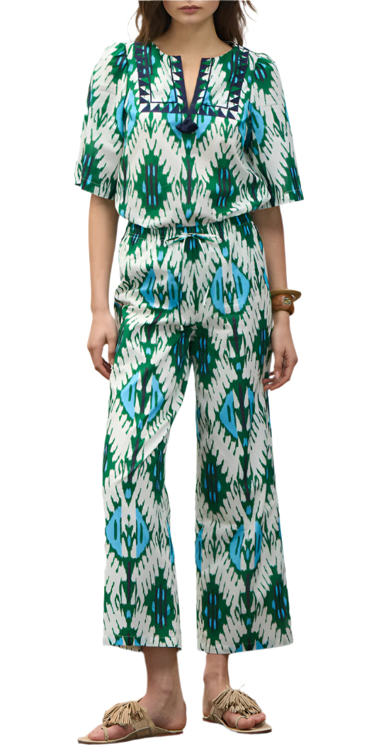 Woman wears the Figue Bodhi Top, a V-neck patterned piece with blue, green, and white geometric designs, paired with fringe sandals and a bracelet.