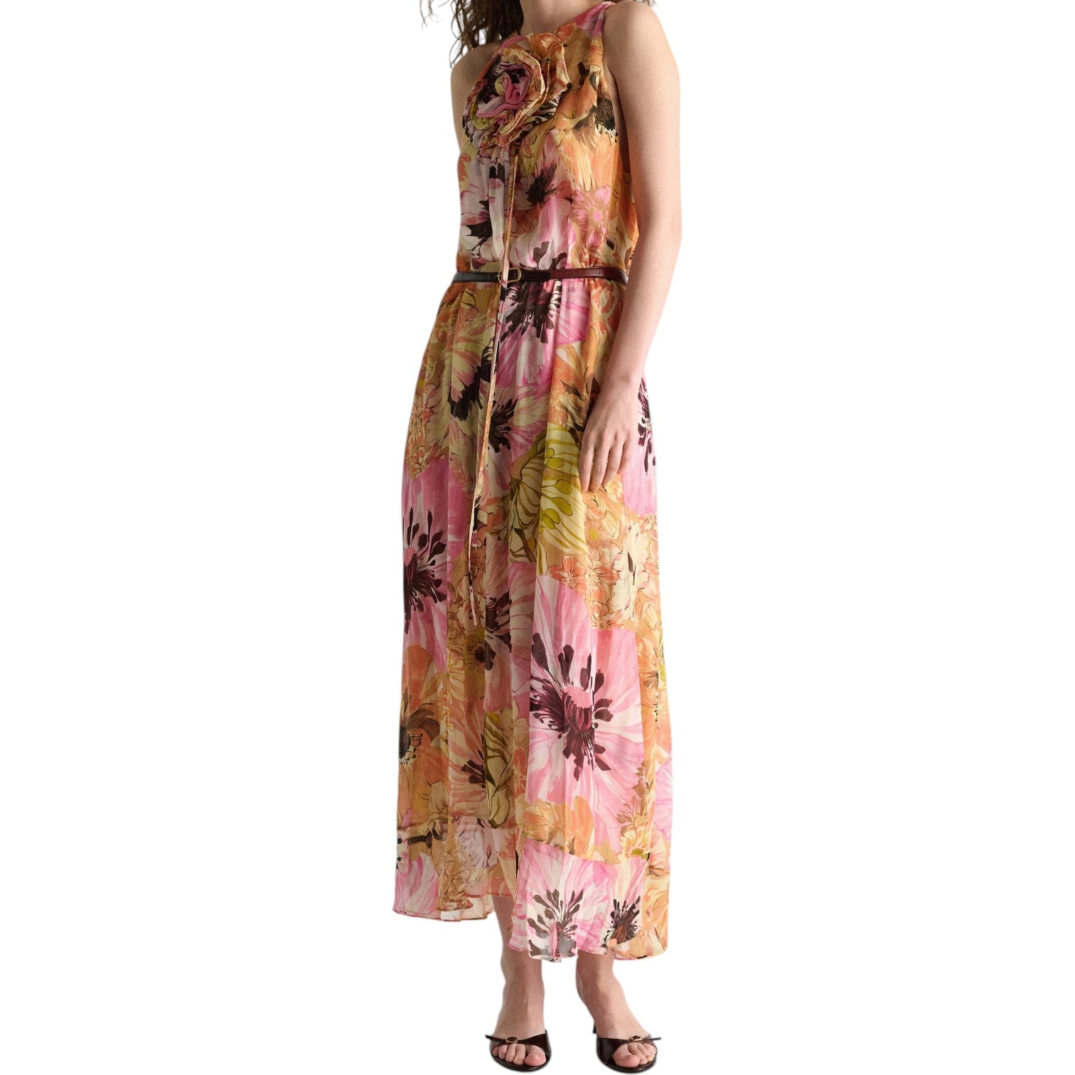 A woman wears Dorothee Schumacher’s Floral Dream Dress—a sleeveless, floor-length A-line in pink, orange, and yellow florals with black accents—paired with black heeled sandals.