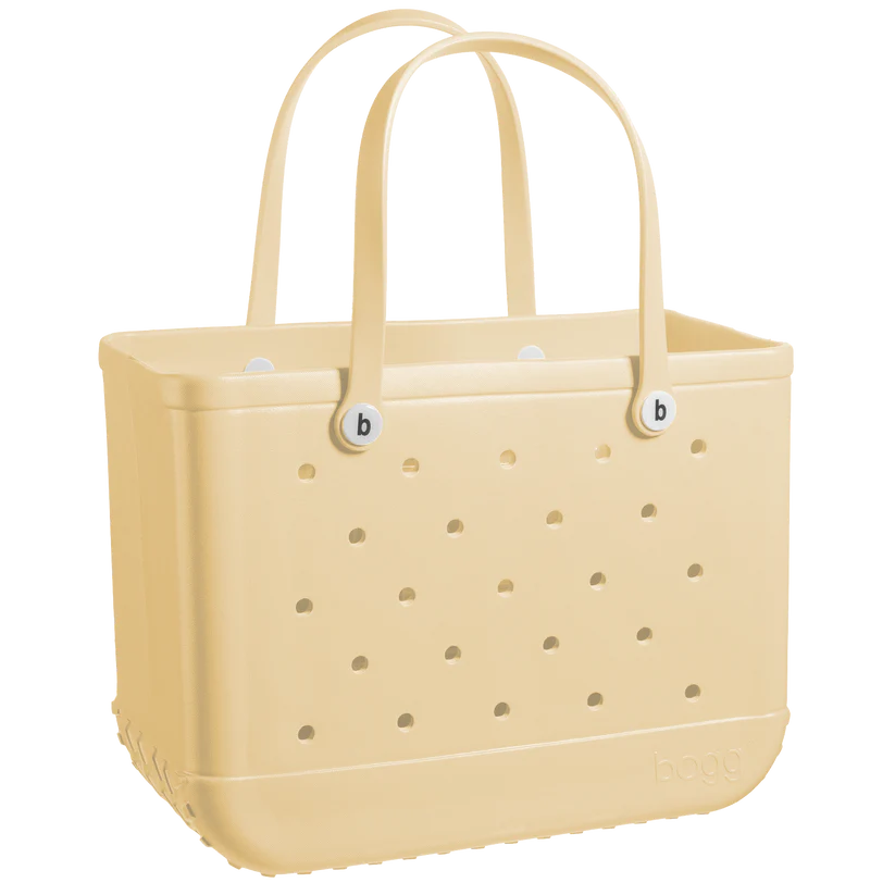 A beige, rectangular Original Bogg Bag tote from Bogg Bags with perforated sides and two sturdy handles. The bag has circular holes arranged in rows, and the brand name "bogg" is embossed on the lower right corner. Known for its durable tote and washable design, it's as practical as it is stylish.