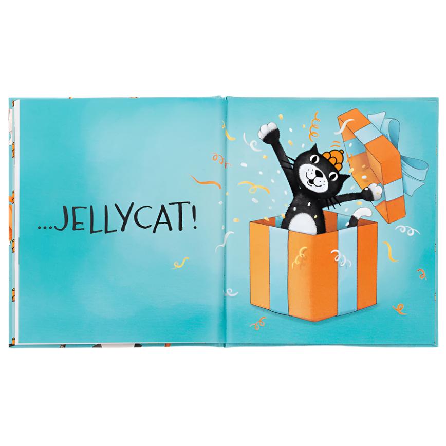 An illustrated page from the Jellycat All Kinds of Cats Book by Jellycat shows a black cat popping joyfully out of an orange and blue striped gift box, with the text "...JELLYCAT!" on the left page. The vibrant pictures and playful rhymes capture the charm of All Kinds of Cats.