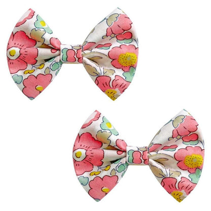 The Milledeux® Small Bowtie Bow Liberty Betsy Q set includes two hair clips featuring a floral design in pink, yellow, and green on a crisp white background from the renowned Liberty of London fabric collection.