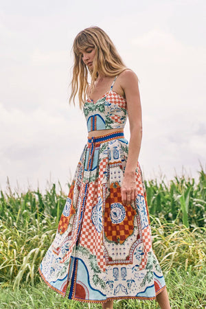 A woman stands outdoors before tall green corn plants on a cloudy day, wearing the Eva Skirt by Hunter Bell NYC in a colorful sundance tile print, crafted from a comfy linen-rayon blend.