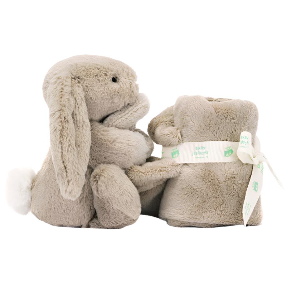 The Jellycat Bashful Beige Bunny Soother by Jellycat features a plush beige rabbit with a white tail, holding a rolled-up beige blanket. The blanket is crafted from recycled fibers and is tied with a white ribbon adorned with green "Baby Planet" logos.