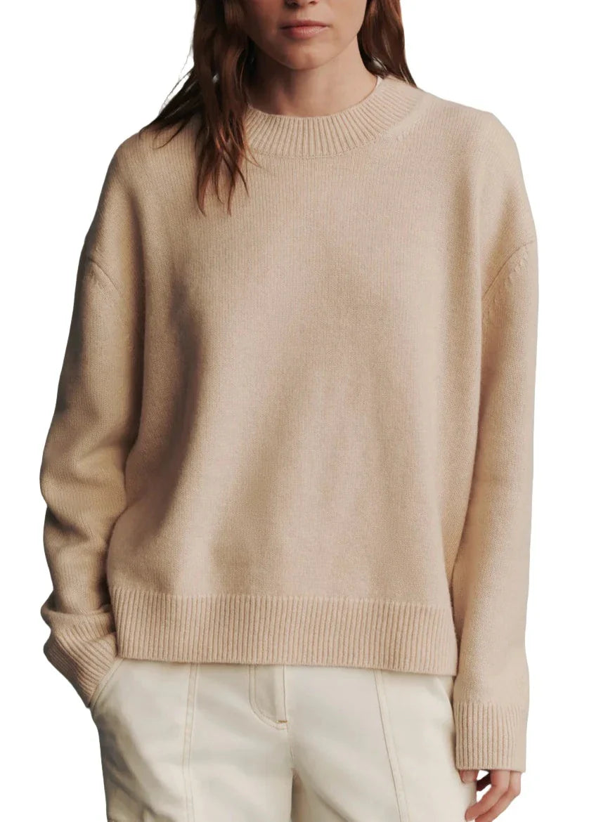 A person wearing a boxy silhouette beige sweater and cream-colored pants stands against a white background. The TWP Boy Cashmere Crew by TWP features a ribbed neckline, cuffs, and hem.