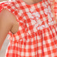 A baby girl is dressed in a charming red gingham dress by Tartine et Chocolat, featuring delicate floral embroidery.