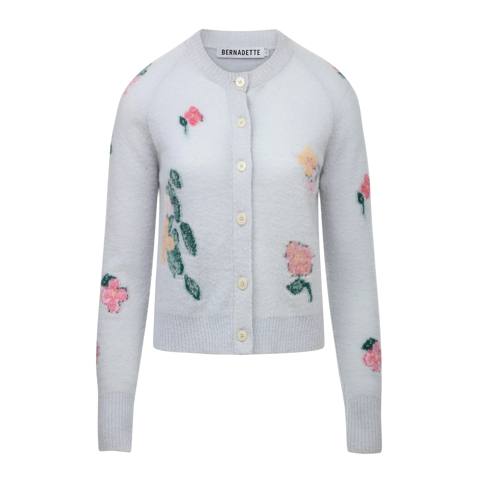 The Clemence Clematis Intarsia Cardigan by Bernadette features a soft wool knit in light blue-grey with a round neck, front buttons, and pink floral patterns, shown against a white background.