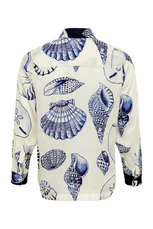 The Carmen Shirt by Carolina K is a long-sleeve top with blue seashells on a white background, seen from the back, inspired by a South African artist collaboration.