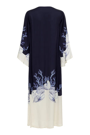 The Lena Kaftan by Carolina K is a long, loose robe with wide sleeves, featuring a navy top and ivory bottom with blue coral and seashell patterns at the hem and cuffs.