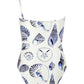 The Maj One Shoulder swimsuit by Carolina K features a white base with blue seashell and marine life prints, inspired by South African artist Felicity Buchanan.