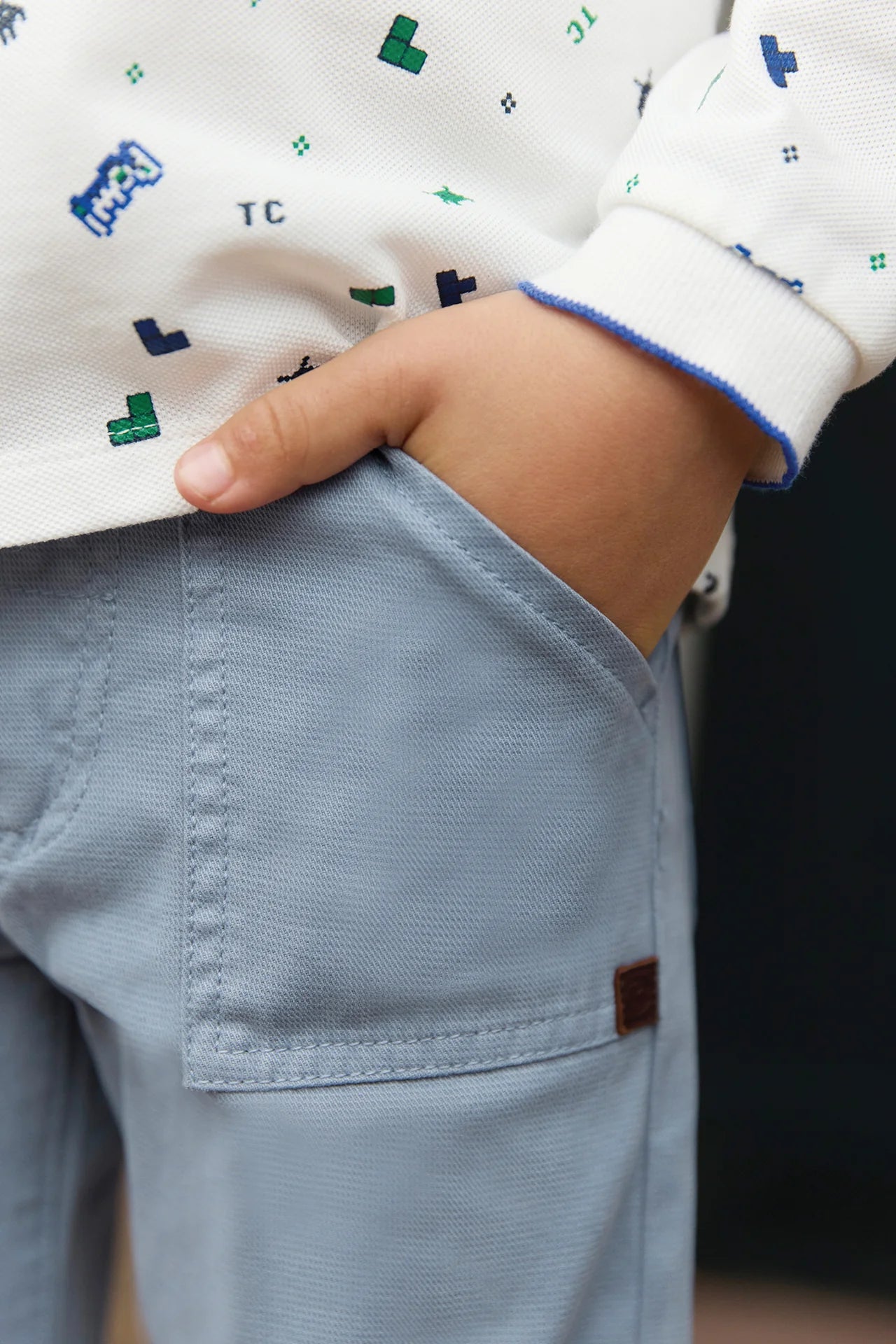 A child from our Tartine et Chocolat Baby Boys' and Boys' Trouser Pants range wears blue-grey trousers and a white patterned shirt, with their right hand tucked stylishly in their pocket.