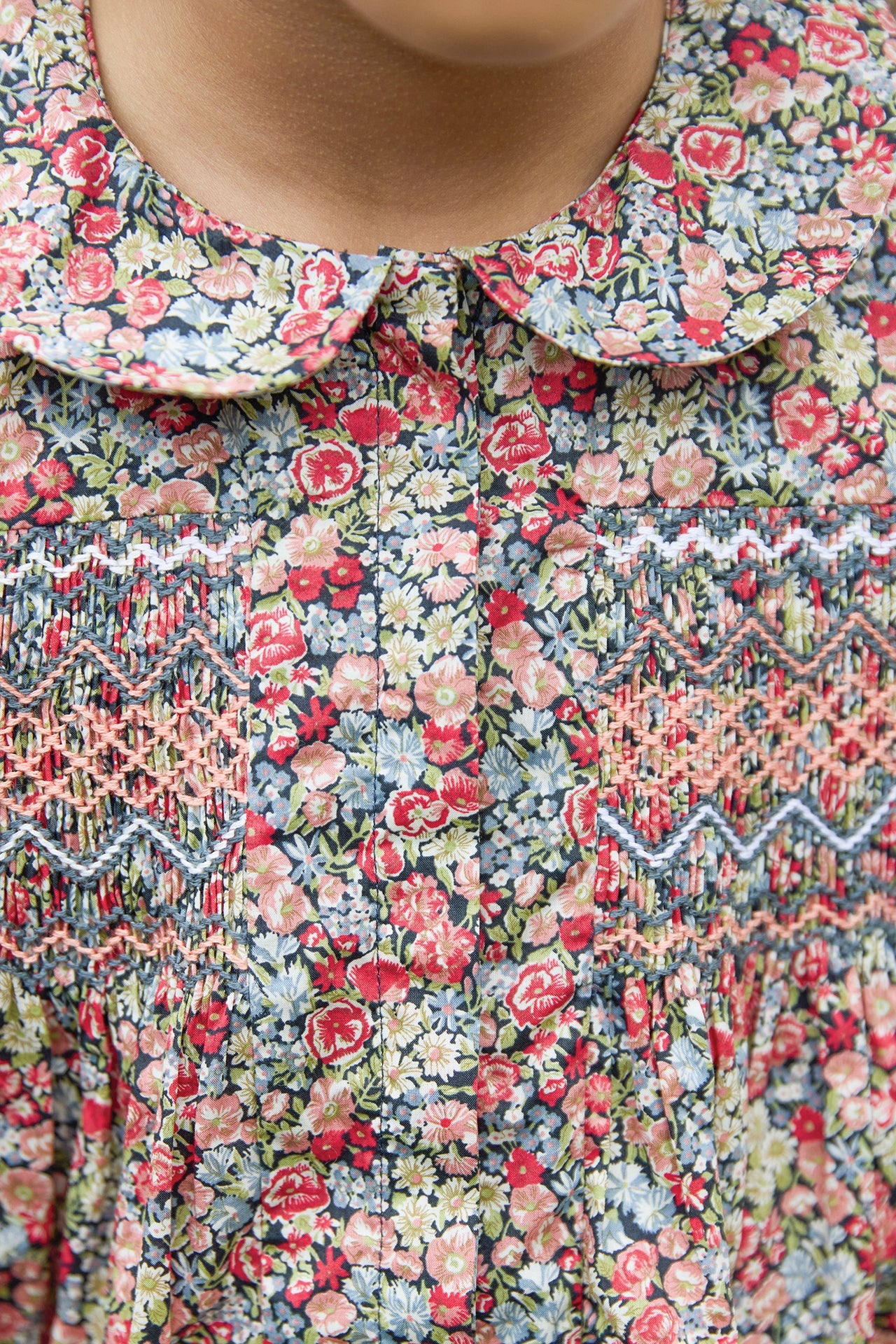 Close-up of the Girls' Liberty Smocked Floral Tunic by Tartine et Chocolat, showing smocked and embroidered details with a rounded collar at the top.
