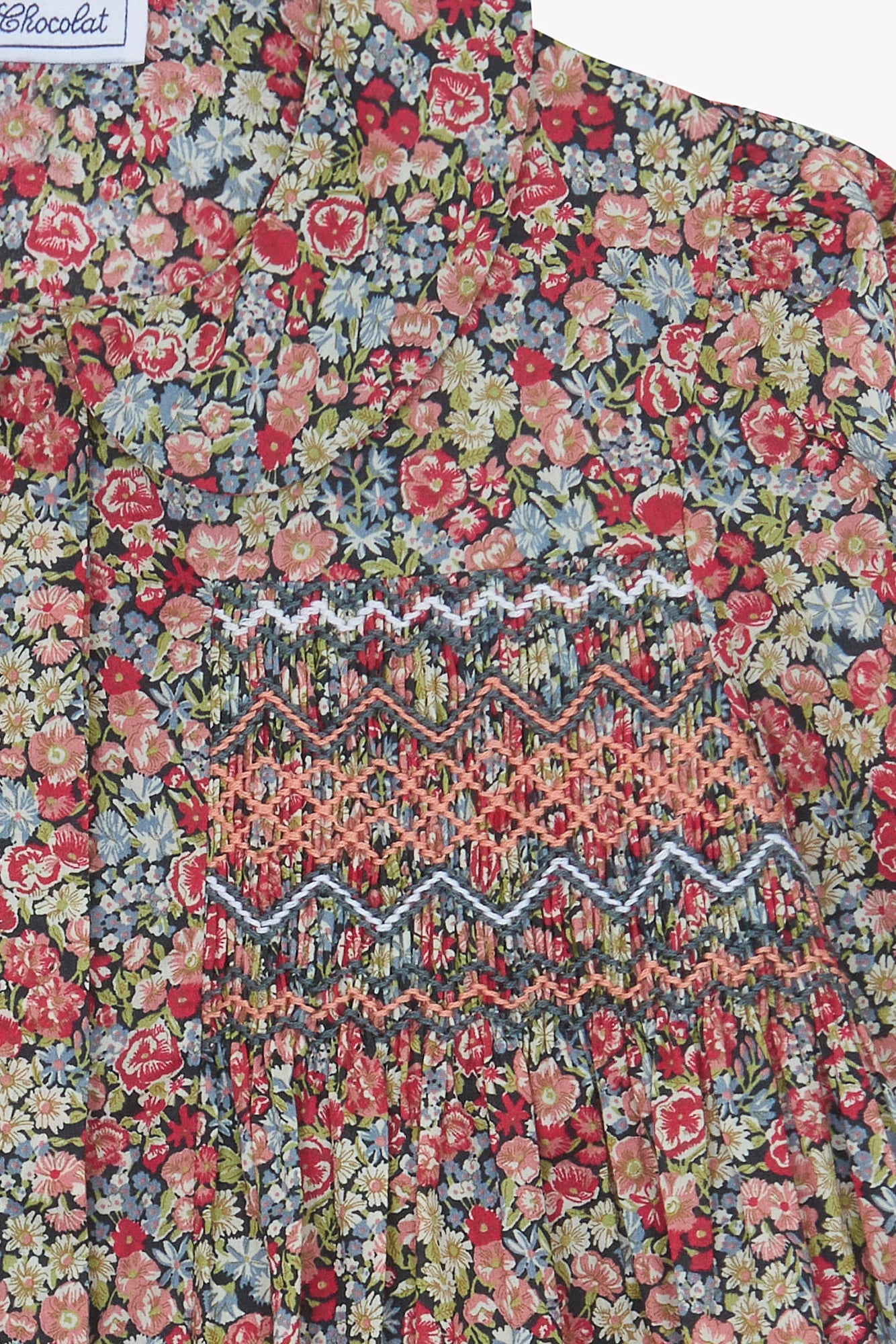 Close-up of the Girls' Liberty Smocked Floral Tunic by Tartine et Chocolat, featuring a colorful floral Liberty print with intricate zigzag smocking—perfect for girls. "Chocolat" label appears in the top left corner.