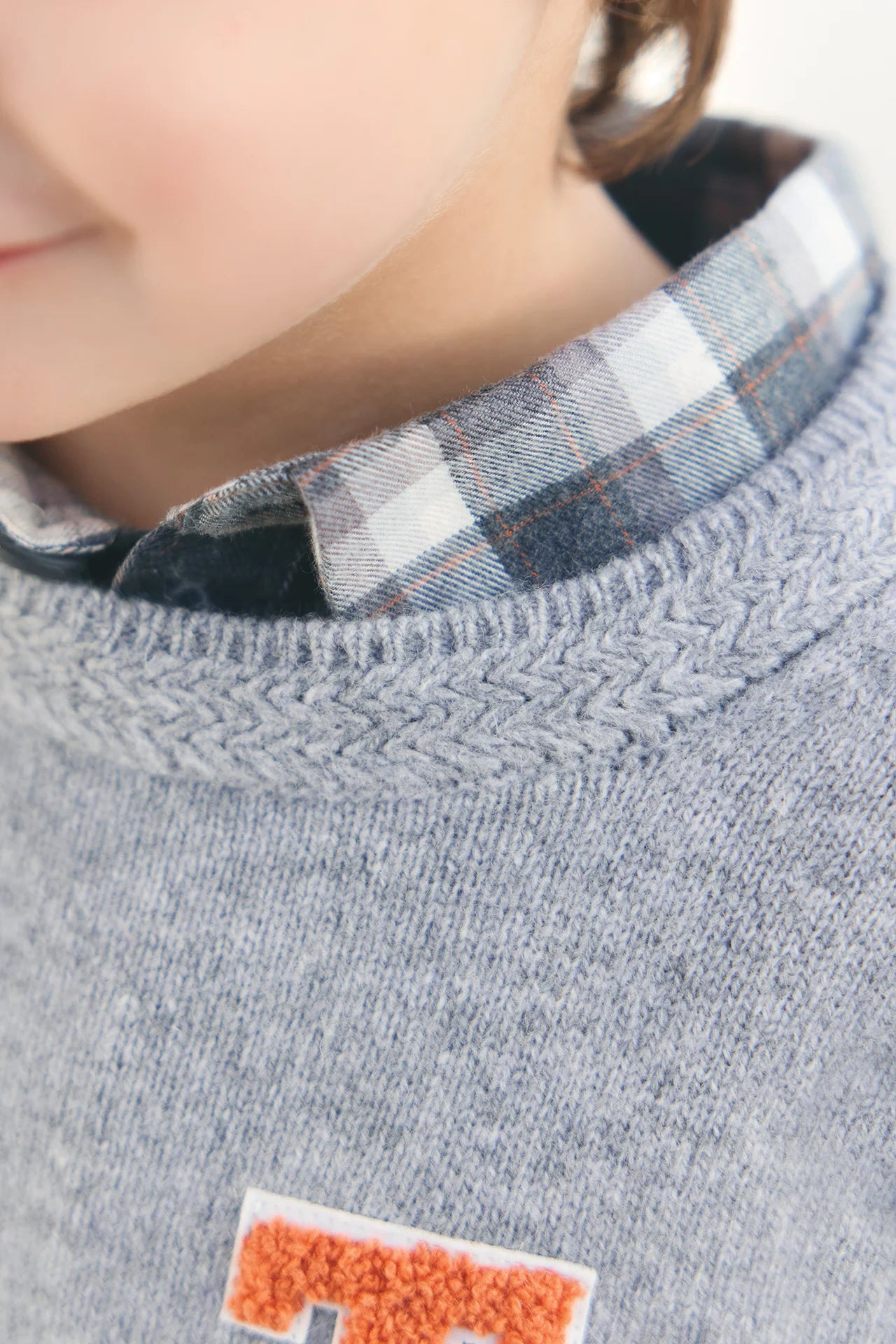 Close-up of a child in the Tartine et Chocolat Boys' Grey China Wool TC Signature Pullover Sweater over a blue and white plaid shirt, highlighting their face and the cozy wool sweater details.
