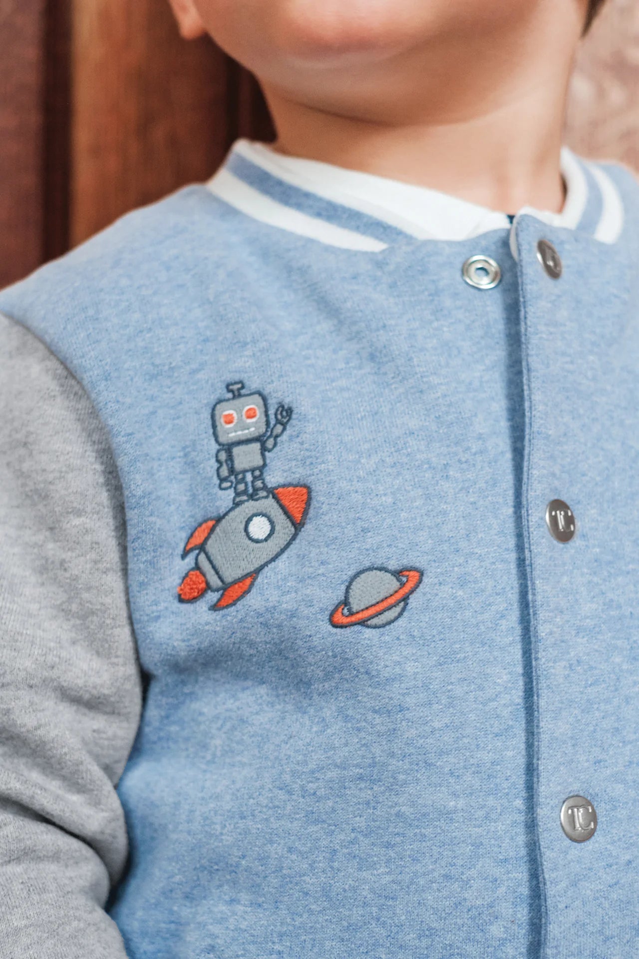 A child wears the Tartine et Chocolat Baby Boys' and Boys' Easy Bomber Cardigan in blue and grey, featuring embroidered robot, rocket, and planet designs.