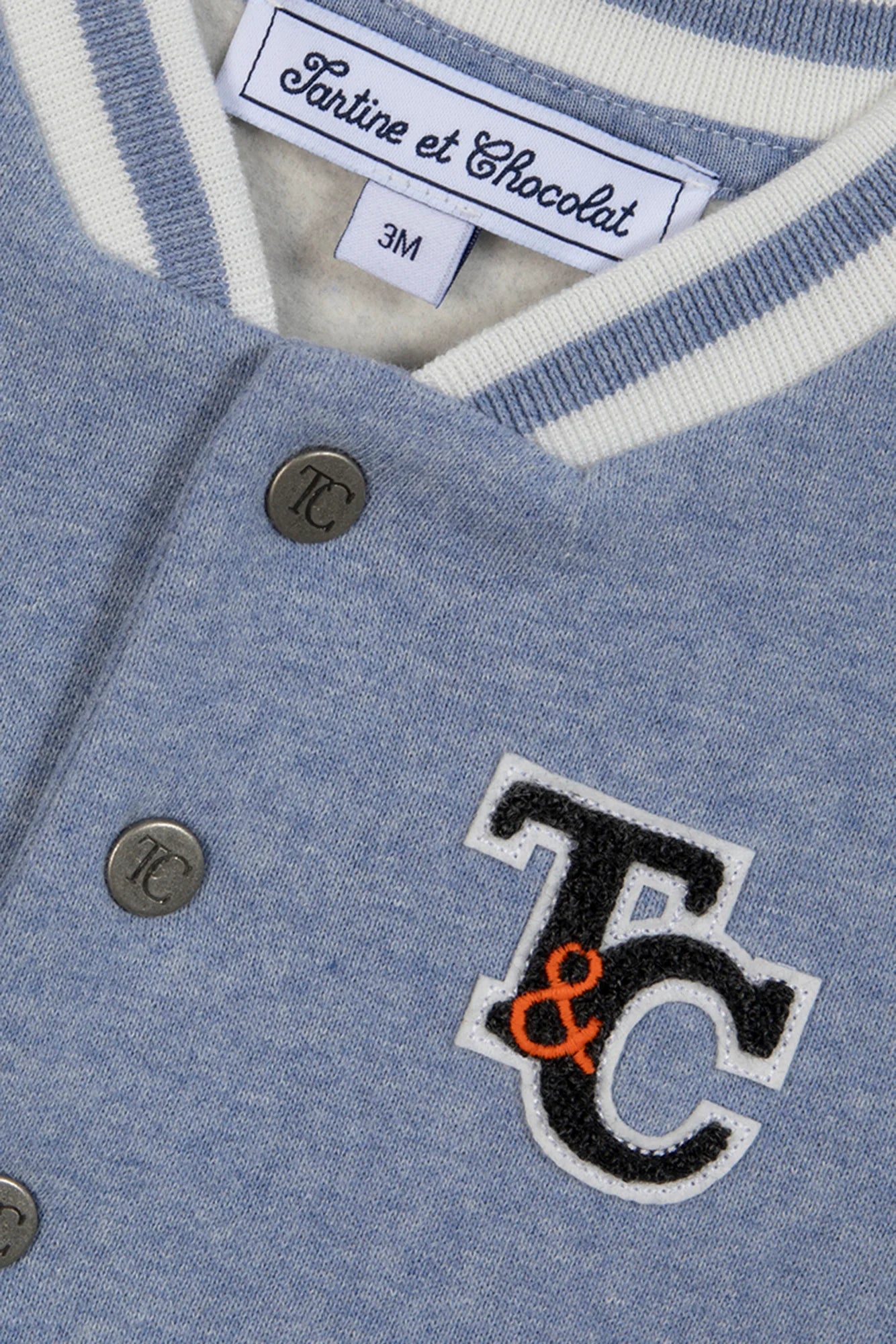 Close-up of Tartine et Chocolat's Baby Boys' and Boys' Easy Bomber Cardigan in blue and white, featuring metal snap buttons, a "TC" patch, and a size 3M label.