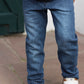 A child in Tartine et Chocolat Baby Boys' and Boys' Cotton Jeans, a white knit sweater, and blue-brown sneakers stands on stone pavement—perfect for everyday wear.