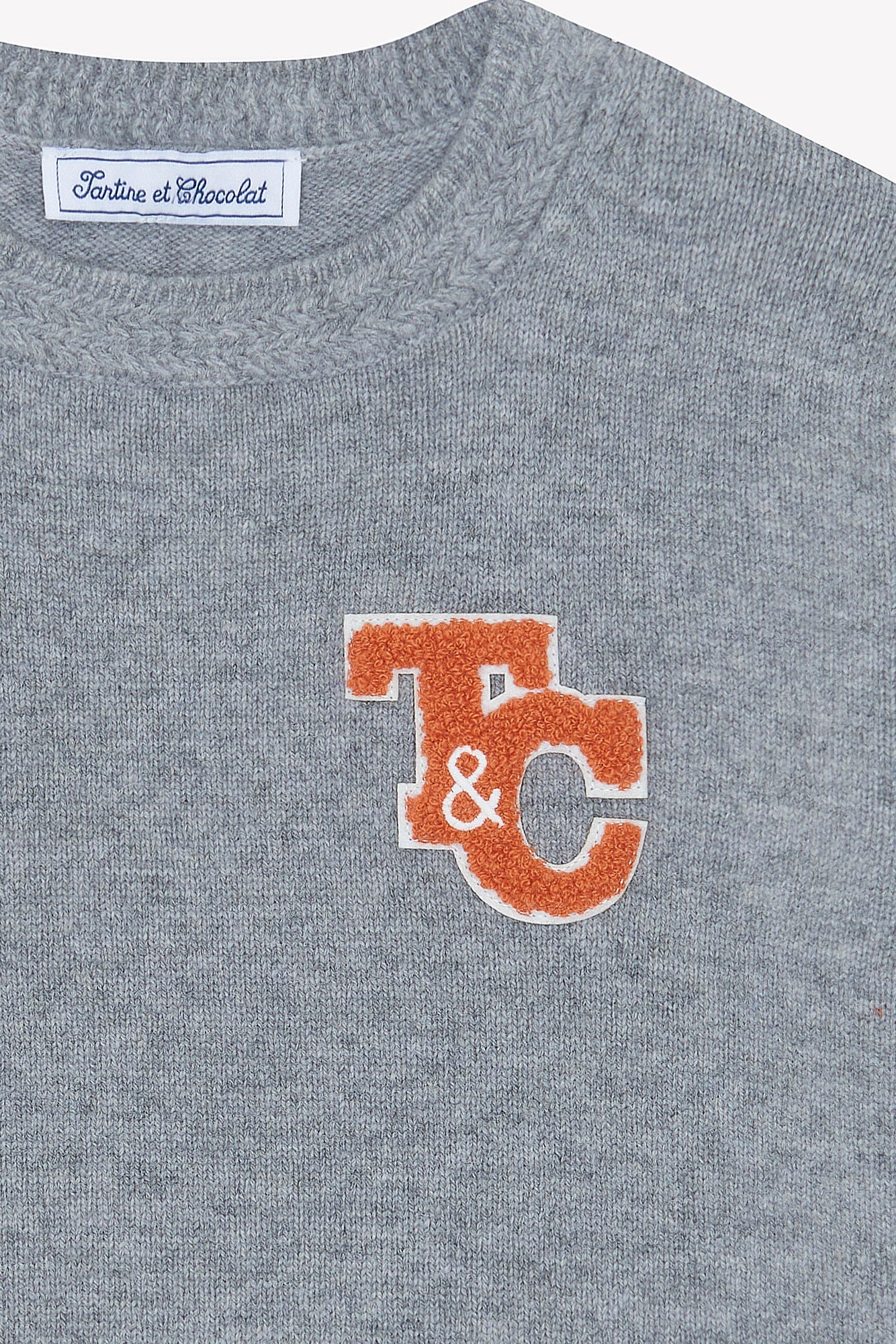 Close-up of the Boys' Grey China Wool TC Signature Pullover Sweater by Tartine et Chocolat, featuring a soft knit, an orange and white "T & C" patch on the chest and a branded label on the neckline.
